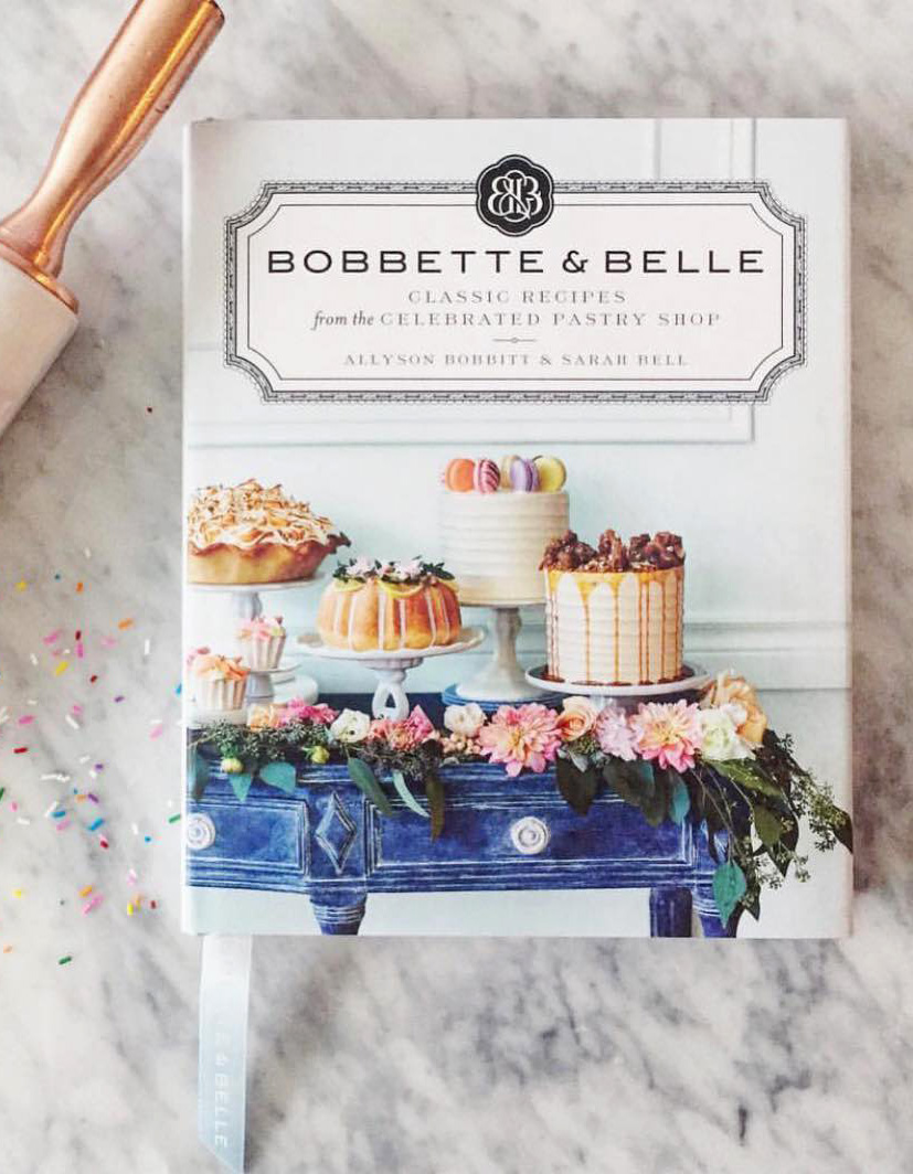 Bobbette & Belle Classic Recipes cookbook displayed on a marble surface with baking confetti and a rolling pin