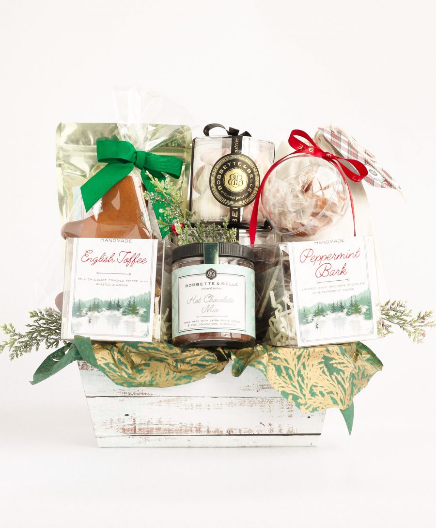 Holiday Joy Gift Basket Toronto A holiday-themed gift basket filled with festive treats, including chocolate cookies, caramel corn, English toffee, peppermint bark, hot chocolate mix, vanilla marshmallows, holiday meringues, a gingerbread cookie, and salted caramels in a bauble.