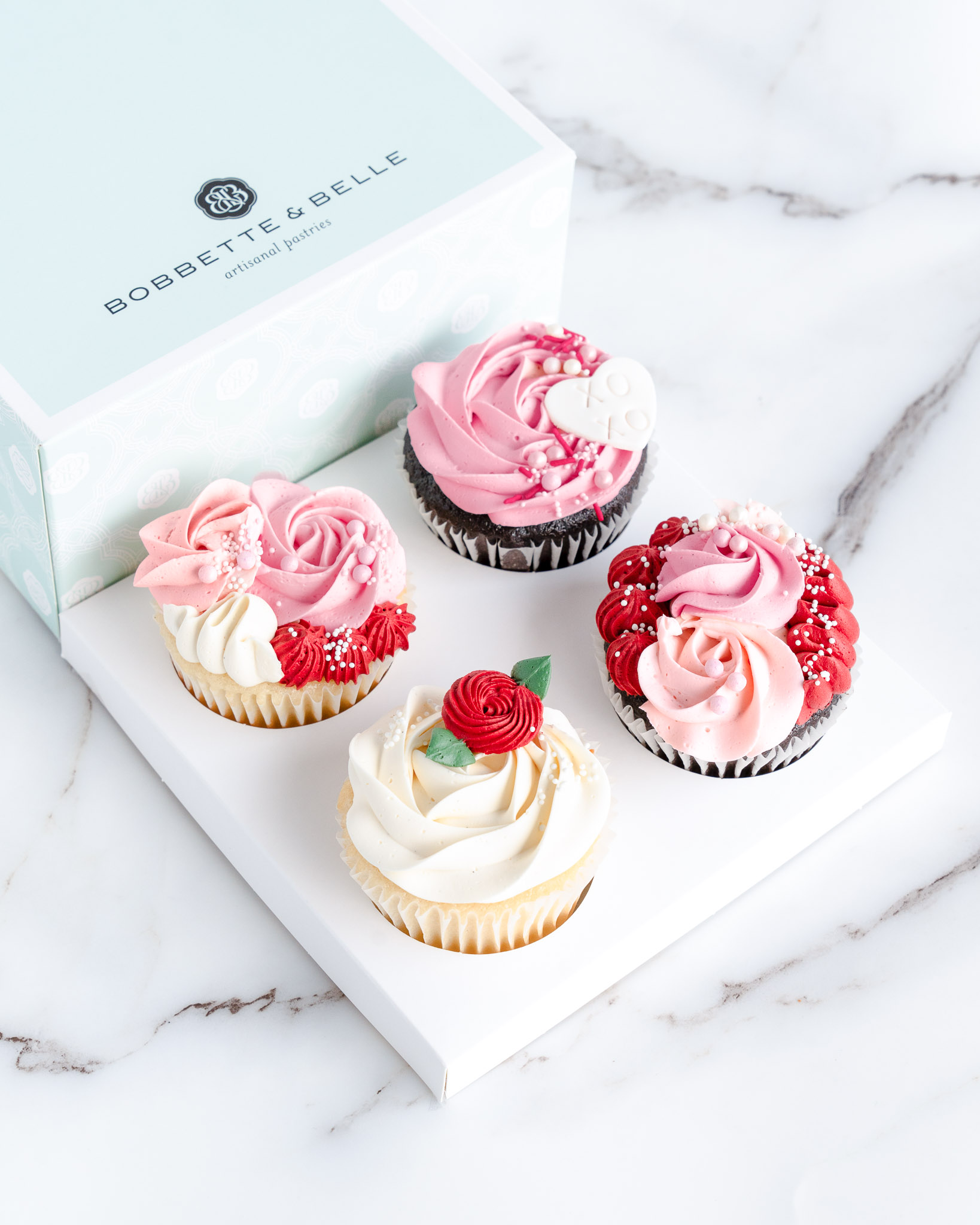 A beautifully arranged Valentine’s Day cupcake gift box featuring four vanilla, red velvet, and chocolate cupcakes, elegantly decorated with handcrafted buttercream florals and romantic detailing.
