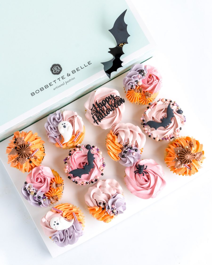 Halloween Cupcakes-2 An open package of 12 decorative Halloween themed cupcakes in shades of orange, pink, purple and black.