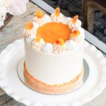 Peaches and Cream Cake topped with peach purée, meringues, buttercream swirls, and fuzzy peach candy on a white plate.