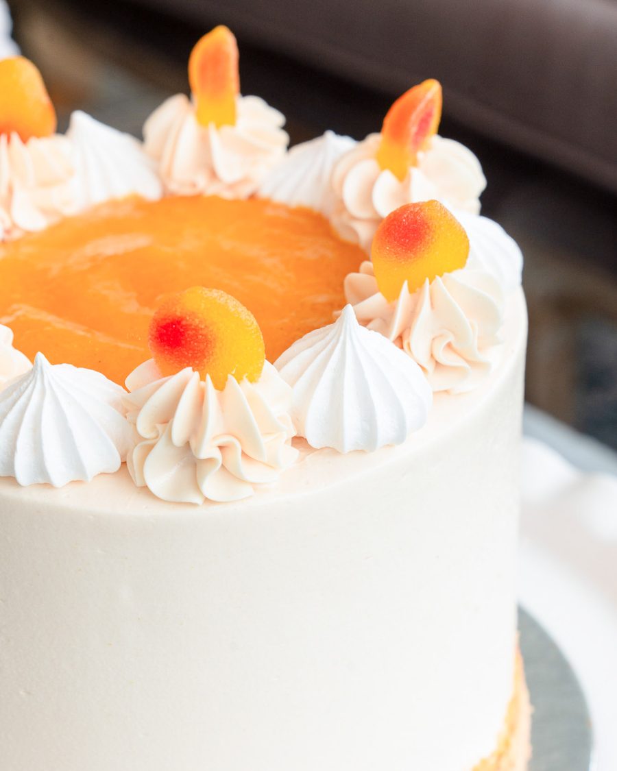 Close-Up of Peaches & Cream Cake Toppings Detailed view of the Peaches and Cream Cake showing peach purée, buttercream swirls, meringues, and fuzzy peach candy.