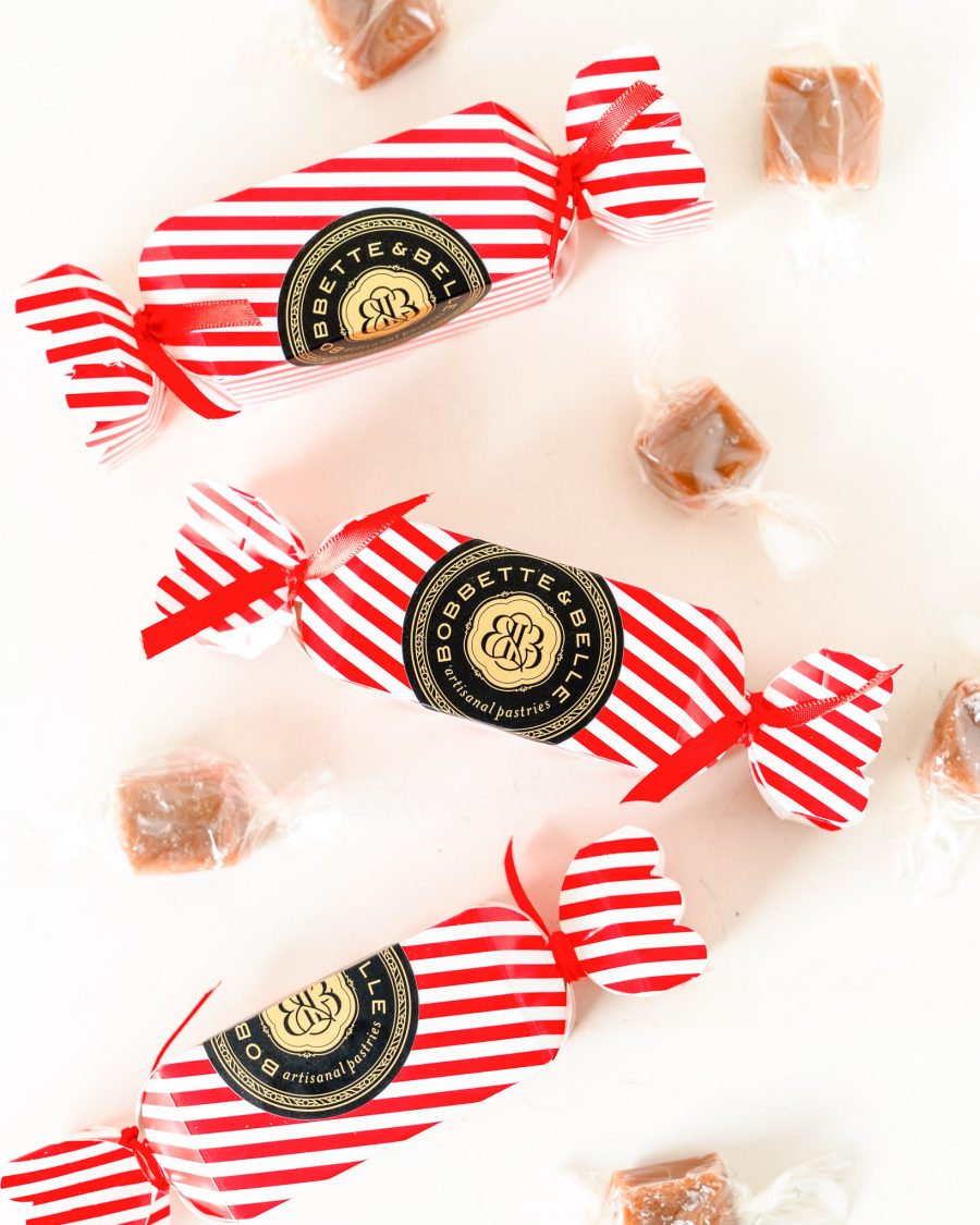 Three festive red-and-white striped Bobbette & Belle holiday caramel crackers surrounded by individually wrapped caramels.