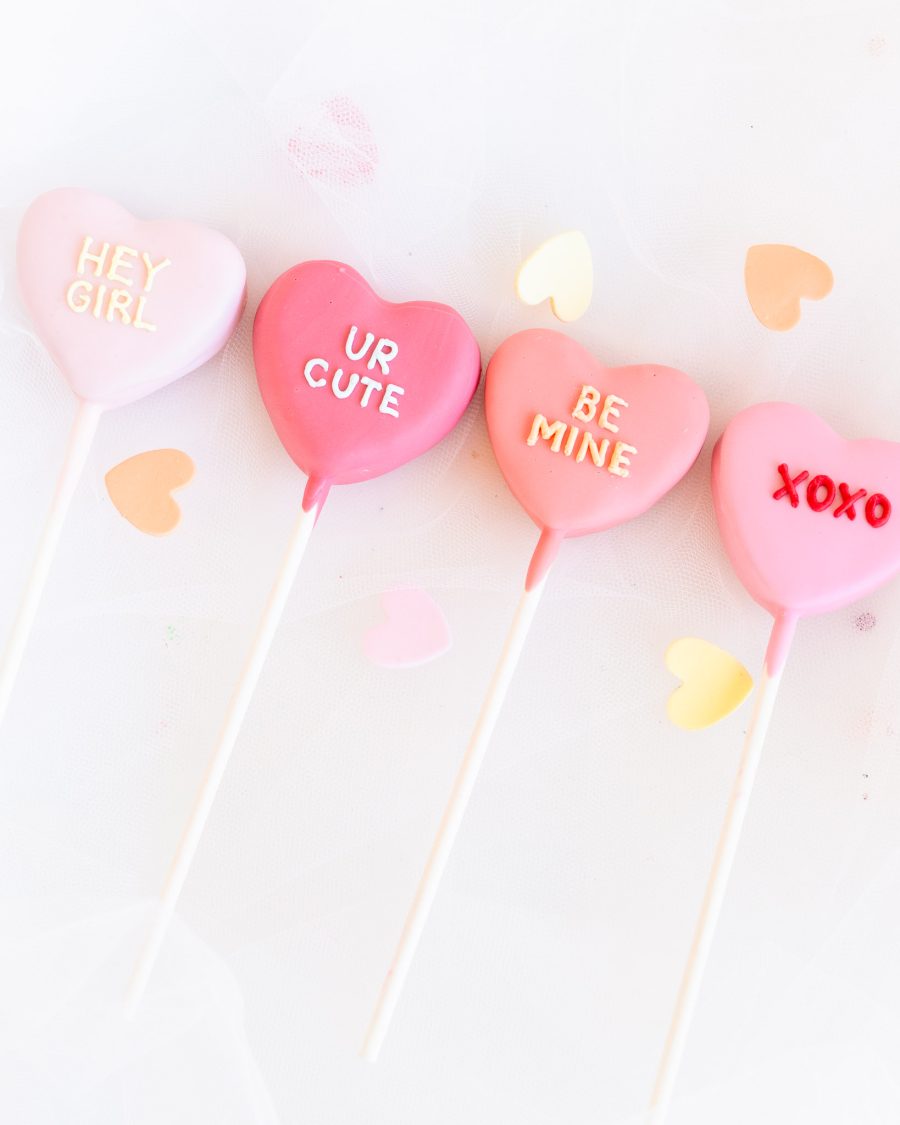 Heart-Shaped Valentine’s Cake Pops – “XOXO” and More Four pink heart-shaped Valentine’s cake pops with messages like “HEY GIRL” and “XOXO”.