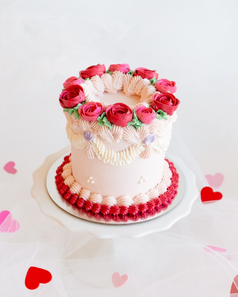 A mini Valentine's cake decorated with red and pink buttercream roses and piped details.